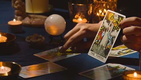 Nahaufnahme-Einer-Frau,-Die-Auf-Einem-Kerzenbeleuchteten-Tisch-Tarotkarten-Liest-Und-Die-Turmkarte-1-Hält
